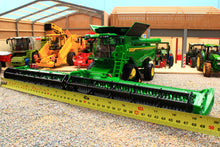 Load image into Gallery viewer, Britains John Deere S7 900 tracked combine harvester model with wide cutting header displayed beside a measuring tape in a farm machinery showroom
