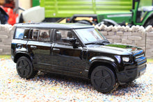 Load image into Gallery viewer, Burago 1 43 scale black Land Rover Defender 110 model displayed on a gravel diorama beside a stone wall and green farm equipment